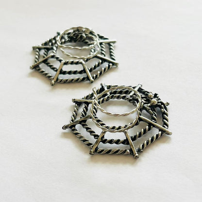 Close-up angled view of twisted metal spider web nipple rings